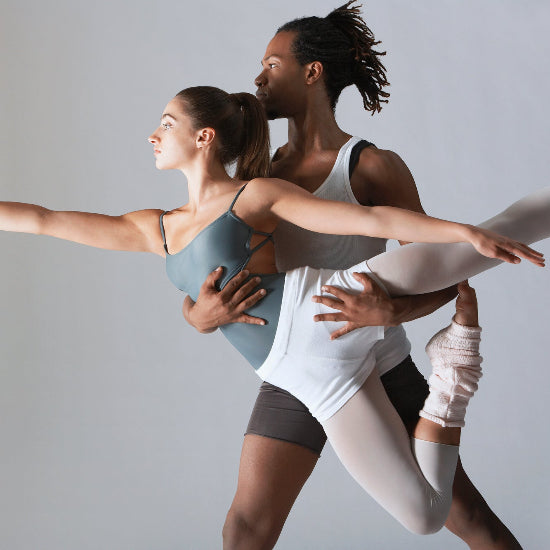 two dancers in a synchronized pose against a plain background