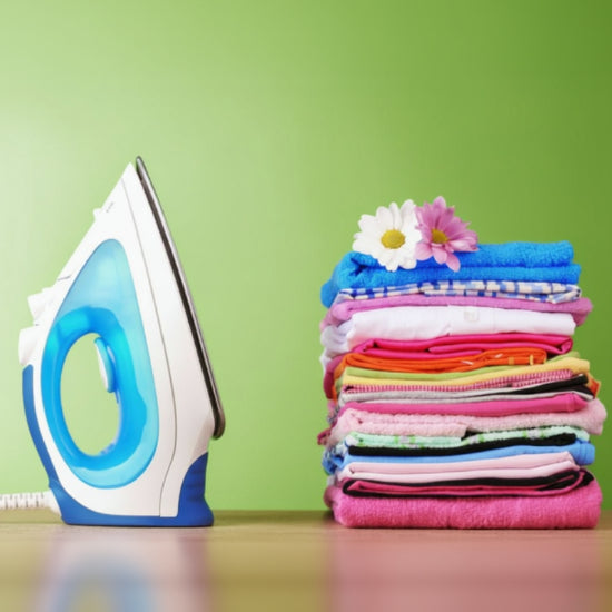 Stack of colorful folded clothes with an iron on a green background