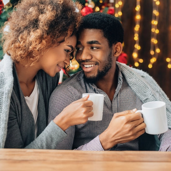 Couple holding mugs together in a cozy setting with Christmas decorations.