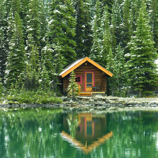 Wooden cabin reflected in a calm lake surrounded by trees