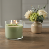 Green candle in a glass holder with a vase of flowers on a wooden surface