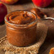 Jar of apple butter on a wooden surface with apples and bread
