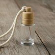 Small clear glass bottle with wooden cap on a string, placed on a wooden surface.