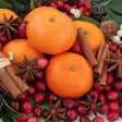 Oranges, cinnamon sticks, and red berries arranged together on a white surface.