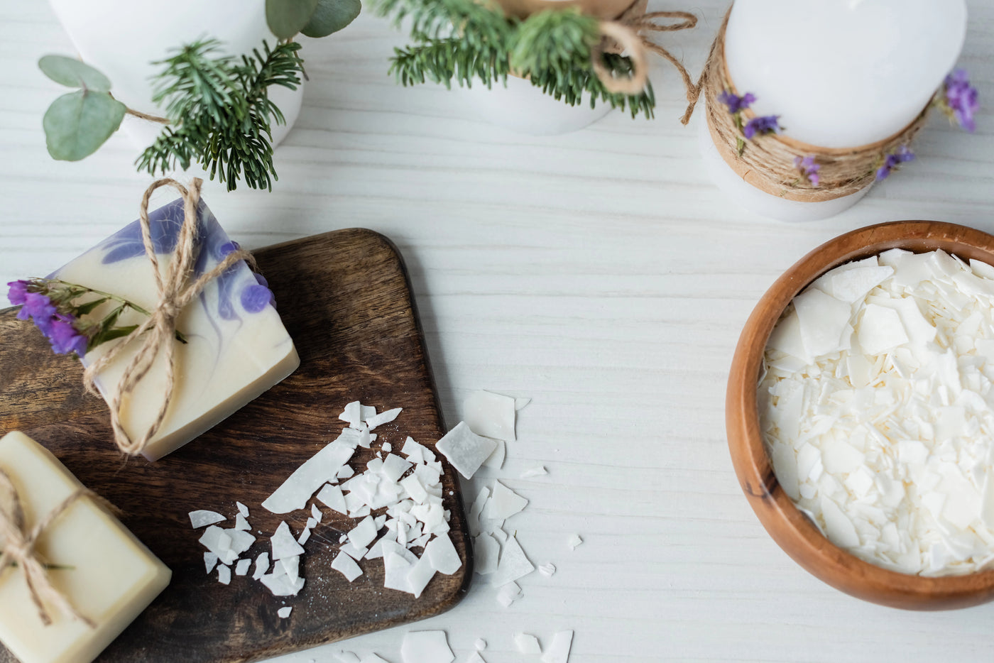 Handmade soap bars on a wooden board with a bowl of wax flakes on a white surface.