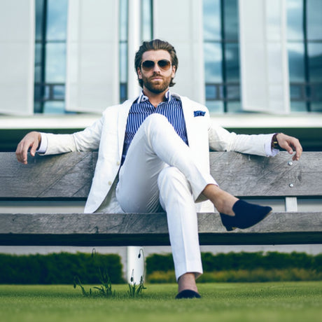 Man in a stylish outfit sitting on a bench with modern building in the background
