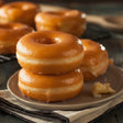 Glistening glazed donuts on a plate with more donuts in the background.