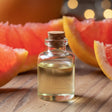 Bottle of grapefruit essential oil with sliced grapefruits on a wooden surface
