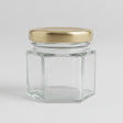 Small hexagonal glass jar with a gold lid on a black background