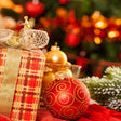 Decorative Christmas scene with ornaments and a gift in front of a blurred tree.
