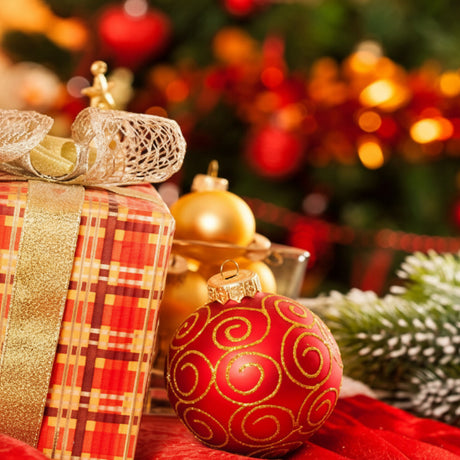 Decorative Christmas scene with ornaments and a gift in front of a blurred tree.