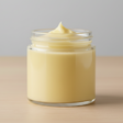 Jar of yellow cream on a beige surface with a gray background