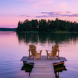 Two wooden chairs on a dock over a lake at sunset.