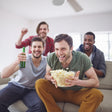 Three men enjoying popcorn and drinks, likely watching a movie or sports event together.