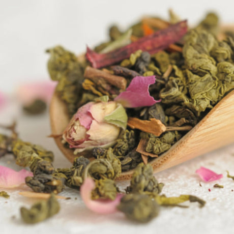 Tea leaves and rose buds in a wooden scoop on a white background