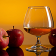 Glass of amber liquid with red apples on a wooden surface and orange background
