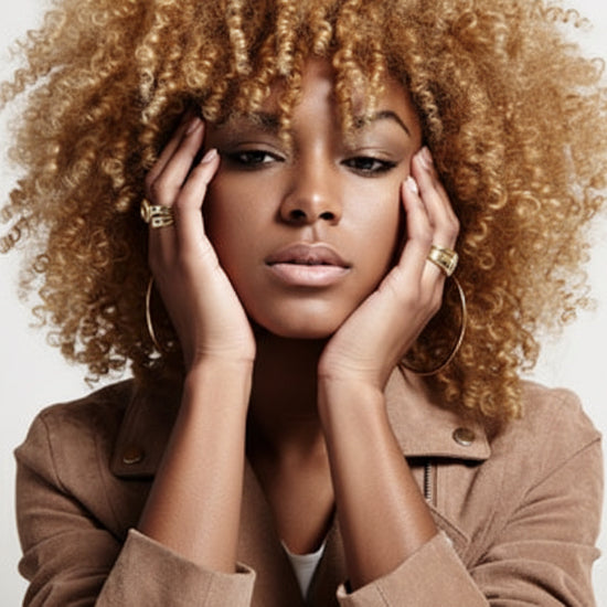 Woman with blonde curly hair wearing a brown jacket against a white background