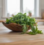 Wooden bowl overflowing with fresh green arugula leaves on a light wooden surface.
