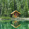 Wooden cabin reflected in a calm lake surrounded by trees