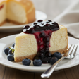 Slice of cheesecake with berry sauce on a plate with blueberries and a fork.