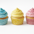 Three cupcakes with buttercream frosting and polka dot wrappers on a white background. sprinkles on the cupcakes match the color of their wrapper
