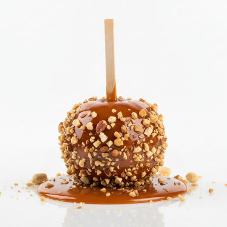 Caramel apple on a stick with nuts on a white background. the apple is set in a puddle of caramel. 