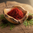 Wooden bowl filled with red saffron threads on a wooden surface with cedar needles and pine cones.