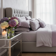 luxurious soft grey and lavender bed with flowers and a candle