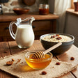 bowl of honey with honey dripper, a pitcher of milk and a bowl of warm oatmeal in a rustic kitchen.