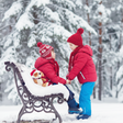 Two children in winter clothing sitting on a bench in a snowy forest.