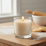 Candle in a glass jar on a wooden surface with a bowl and rolling pin in the background