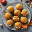 Pumpkin whoopie pies on a plate with pumpkins and a cup of tea in the background