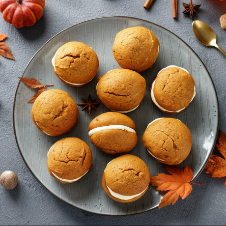Pumpkin whoopie pies on a plate with pumpkins and a cup of tea in the background
